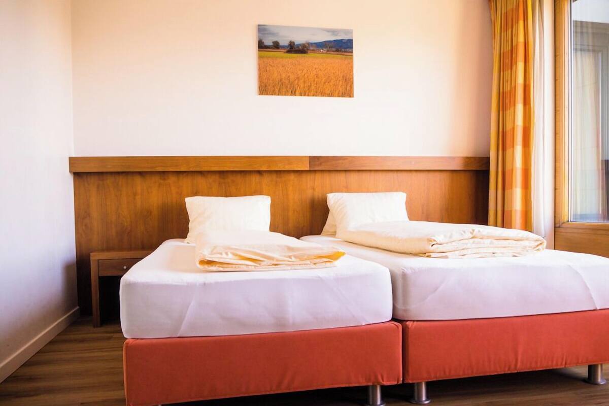 Ein Doppelzimmer mit zwei Betten, einem Holzkopfteil und einem Wandbild einer Landschaft.