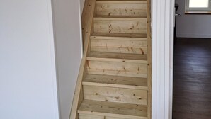A wooden staircase with white walls and a door leading to another room.