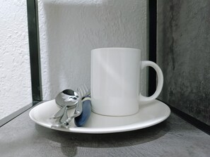 A white mug on a white saucer with a spoon and a fork on a dark surface. - Nomad Inn Guest House (Bishkek)