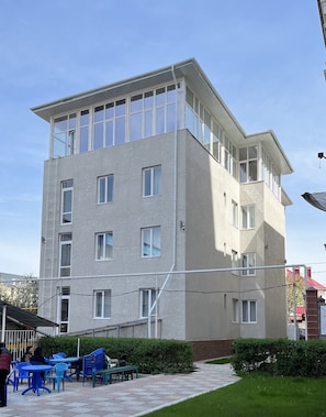 A multi-story building with a flat roof, large windows, and a paved courtyard with outdoor seating. - Nomad Inn Guest House (Bishkek)