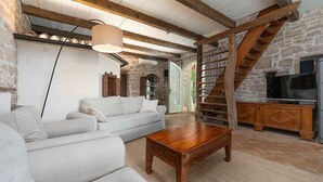 A spacious living room with a white sofa, wooden coffee table, and a stone wall. A staircase leads to a loft area with a TV. - Nice home in Sveti Lovrec (Sveti Lovrec)