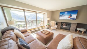A living room with a large sofa, a fireplace, and a television displaying a mountain scene. - Saints John 2537 (Keystone)