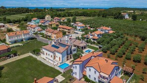 Ett bostadsområde med hus som har röda tegeltak, en swimmingpool och utsikt över havet.