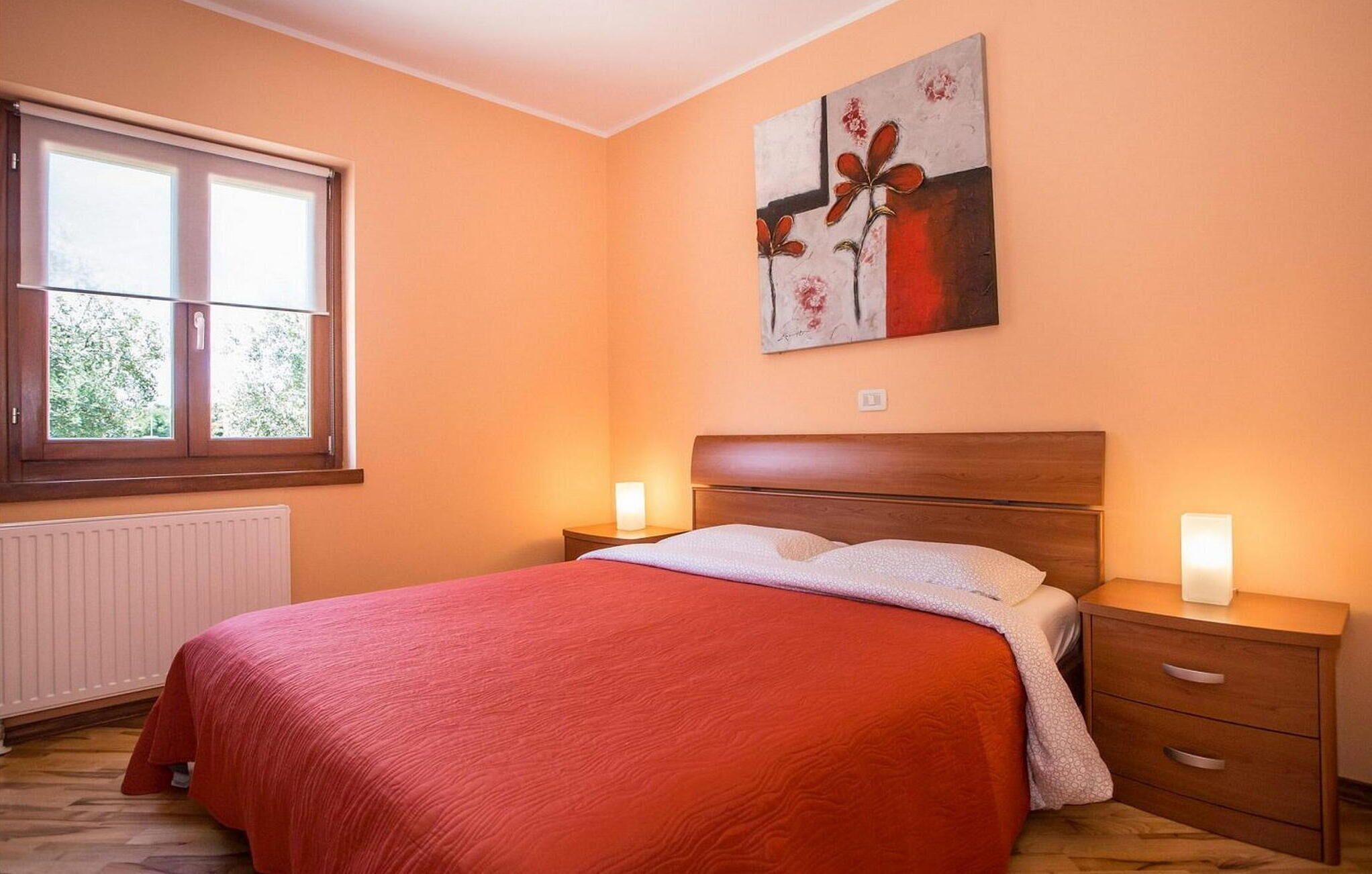 Ein Schlafzimmer mit einem Bett, zwei Nachttischen, einem Fenster und einem Bild an der Wand.