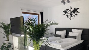 A modern bedroom with a bed, a TV on a stand, and potted plants. - Studio Apartment mit Balkon, am See mit Privat Badestrand. Haustierfreundlich! (Afritz)