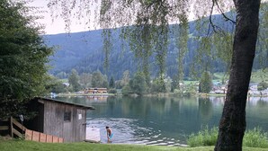 A lakeside cabin with a dock extending into the water, surrounded by lush greenery and mountains in the background. - Studio Apartment mit Balkon, am See mit Privat Badestrand. Haustierfreundlich! (Afritz)
