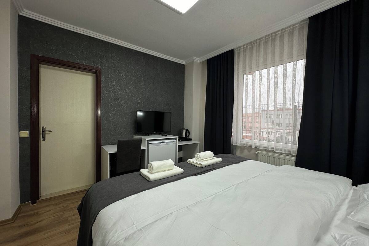 A hotel room with a bed, a desk with a television, a coffee machine, and a window with curtains.