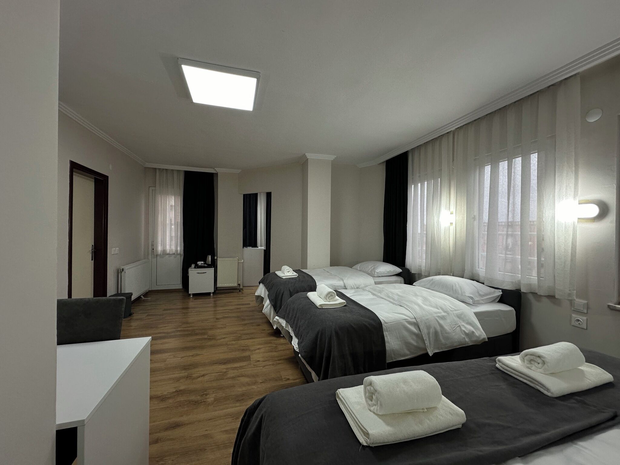 Hotellihuone, jossa on kaksi sänkyä, työpöytä, patteri ja ikkuna, jossa on verhot.