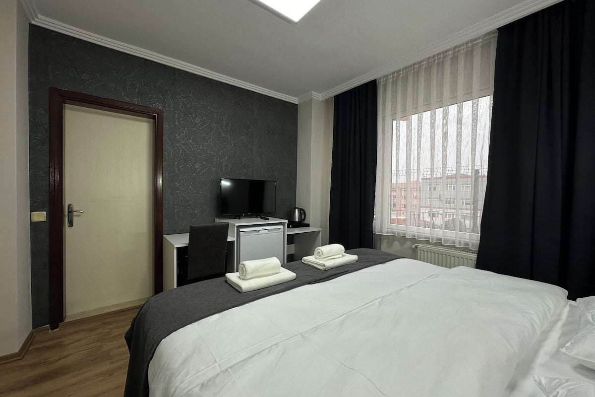 A hotel room with a bed, a desk with a television, a coffee machine, and a window with curtains.