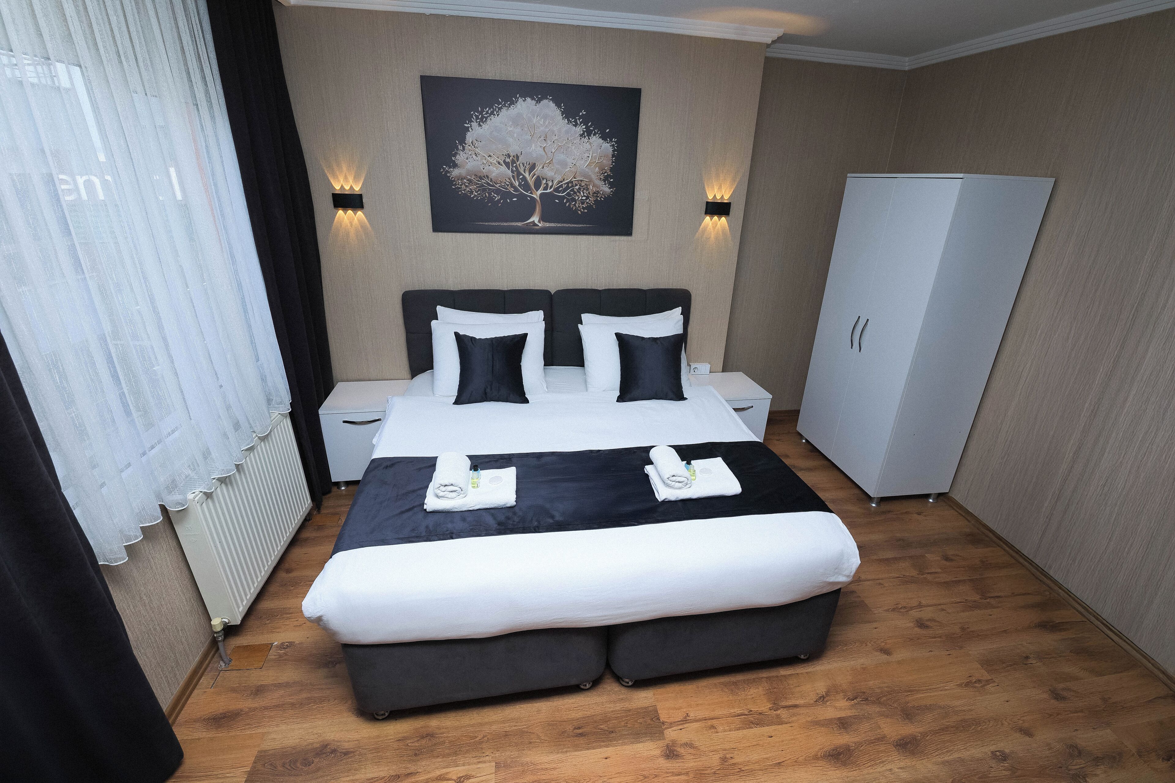 Una habitación de hotel con una cama grande, dos mesitas de noche, un armario y una obra de arte colgada en la pared.