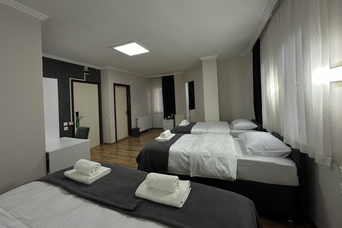 Ett hotellrum med tre sängar, ett litet skrivbord, en spegel och ett fönster med gardiner.