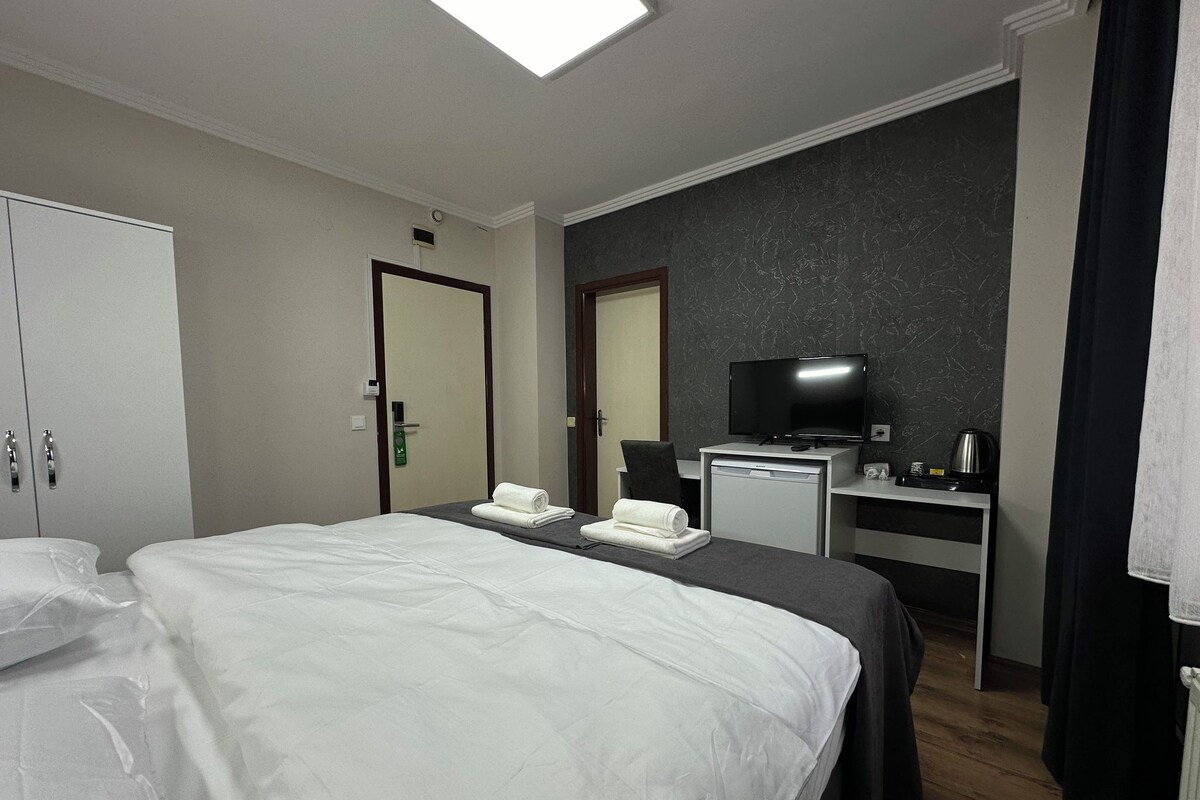 A hotel room with two beds, a desk with a television, and a small kitchenette.