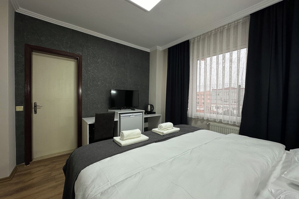 A hotel room with a bed, a desk with a television, a coffee machine, and a window with curtains.