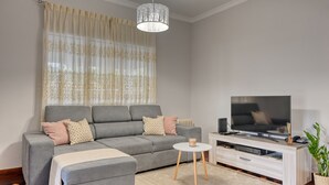 A modern living room with a grey sofa, a white coffee table, a flat-screen TV, and a decorative pendant light. - Villa Rosa, a Home in Madeira (Funchal)