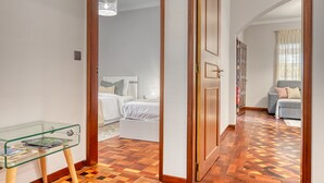 A hotel room with a wooden parquet floor, a glass table with magazines, a bed with white bedding, and a small seating area with a sofa and cushions. - Villa Rosa, a Home in Madeira (Funchal)