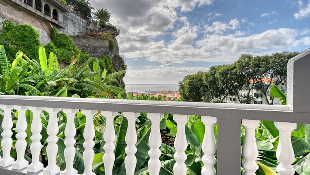 A balcony with white balustrades overlooking lush greenery and a stone wall. - Villa Rosa, a Home in Madeira (Funchal)