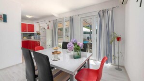 Une cuisine moderne avec des meubles rouges, une table à manger blanche et une vue sur l’extérieur grâce à de grandes fenêtres.