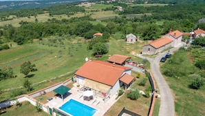 Un quartier résidentiel doté d’une piscine, de plusieurs maisons aux toits recouverts de tuiles rouges et entouré de champs verdoyants.