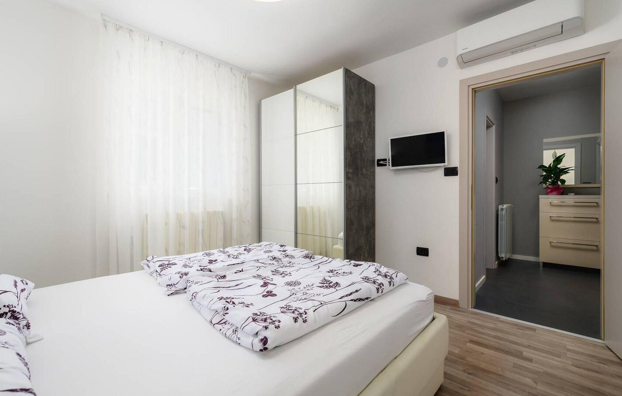 Een moderne slaapkamer met een bed, een aan de muur bevestigde televisie, een spiegel en een deur naar een badkamer.