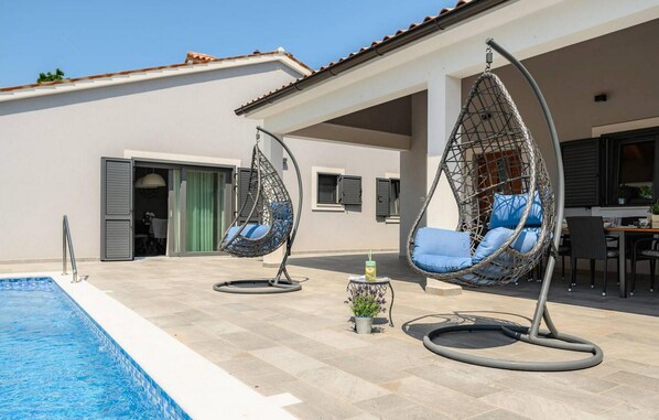 A poolside area with two hanging chairs, a small table with a drink, and a potted plant. - Gorgeous home in Labin (Labin)