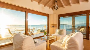 A spacious room with large windows overlooking a pool and the sea, featuring white furniture and a wooden ceiling. - Beachfront 'Karavi Villa': 270° Views & Sea Access (Sivota)