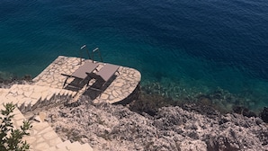 A coastal view with a stone deck and lounge chairs overlooking the sea. - Beachfront 'Karavi Villa': 270° Views & Sea Access (Sivota)