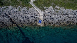 An aerial view of a rocky coastline with a stone pathway leading to a small dock with two blue lounge chairs. - Beachfront 'Karavi Villa': 270° Views & Sea Access (Sivota)