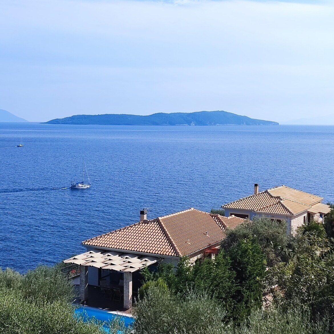 Uma villa costeira com piscina, telhados de terracota e vista para o mar.