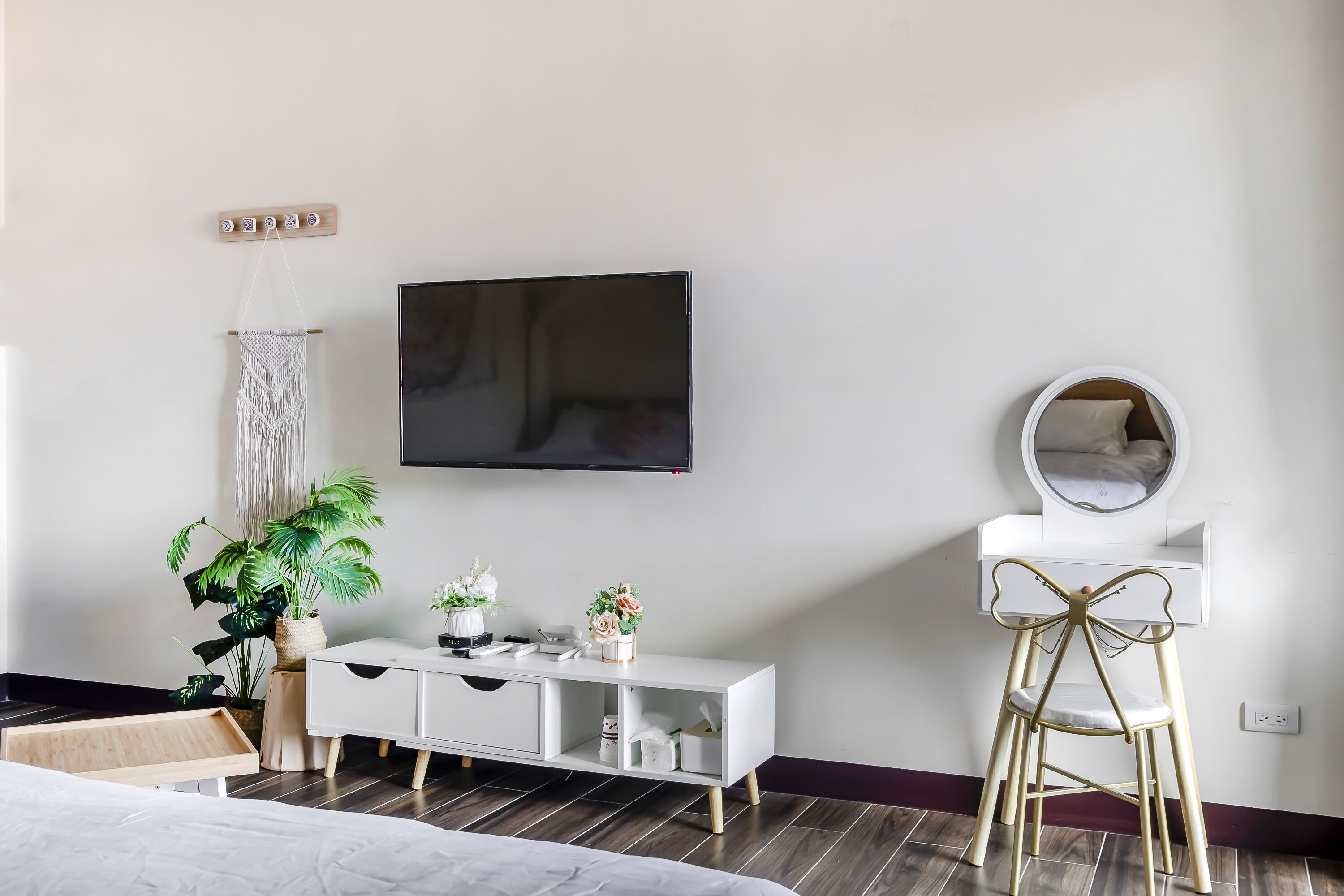 Een moderne slaapkamer met een bed, een witte dressoir, een televisie, een spiegel en een potplant.