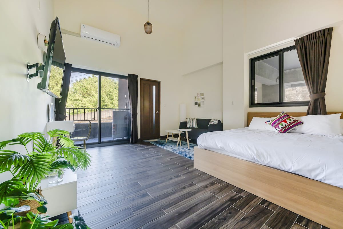 A modern hotel room with a large bed, a desk, and a balcony.