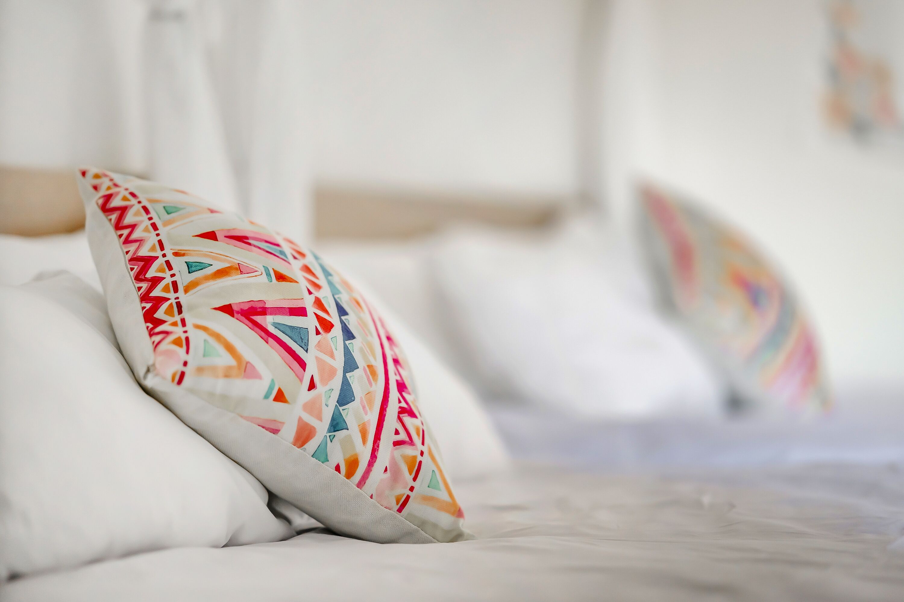A bed with white bedding and colorful patterned pillows.