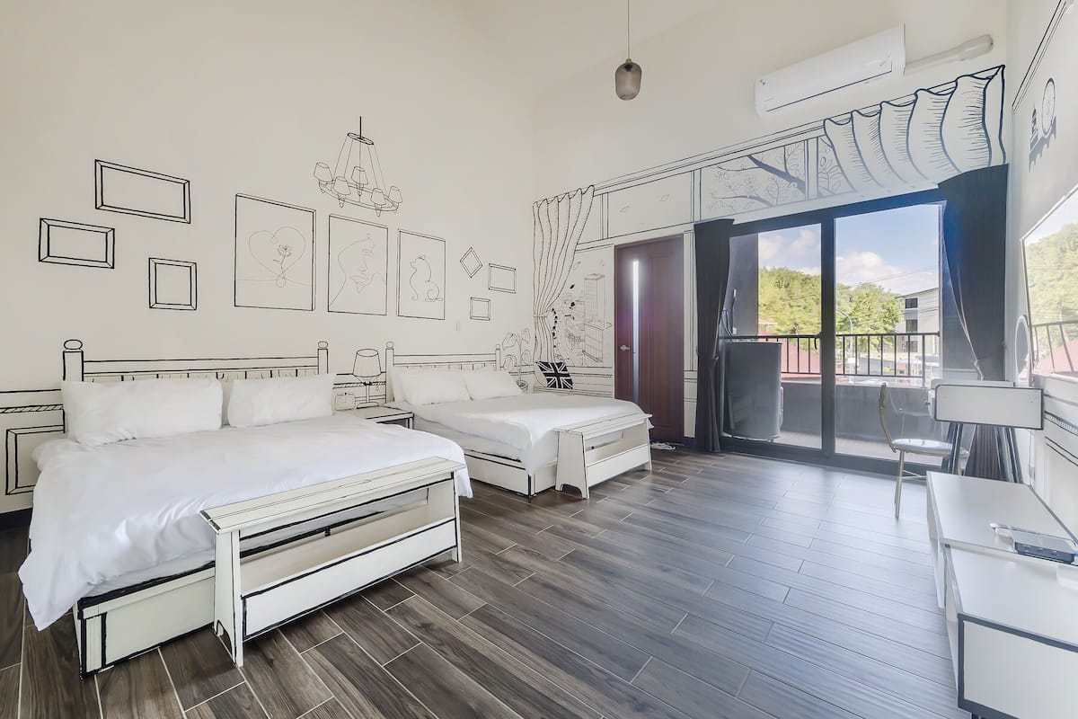 A bedroom with two beds, a desk, and a balcony with a view.