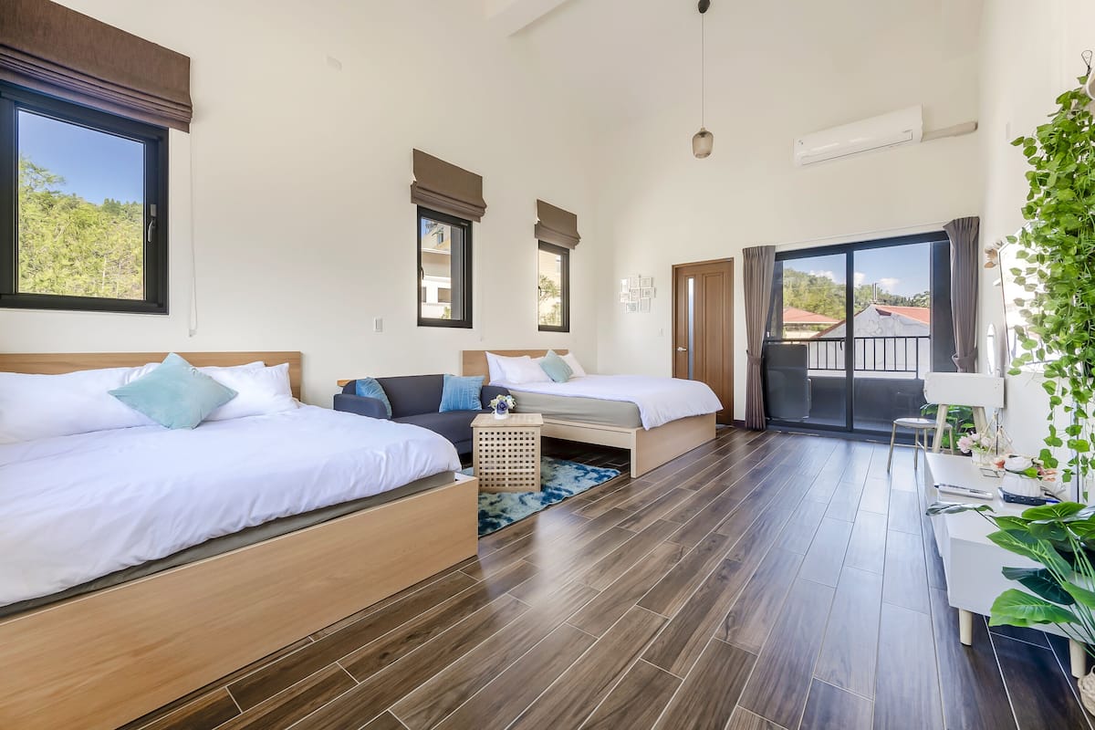 A modern hotel room with two beds, a small seating area, and a balcony with a view.