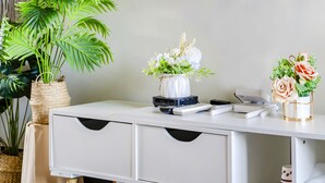 Et hvidt skrivebord med en flettet kurv, en potteplante, en vase med hvide blomster og en vase med lyserøde blomster.