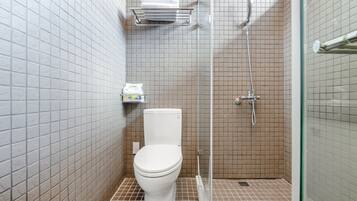A small, tiled bathroom with a toilet, a shower, and a shelf with toiletries.