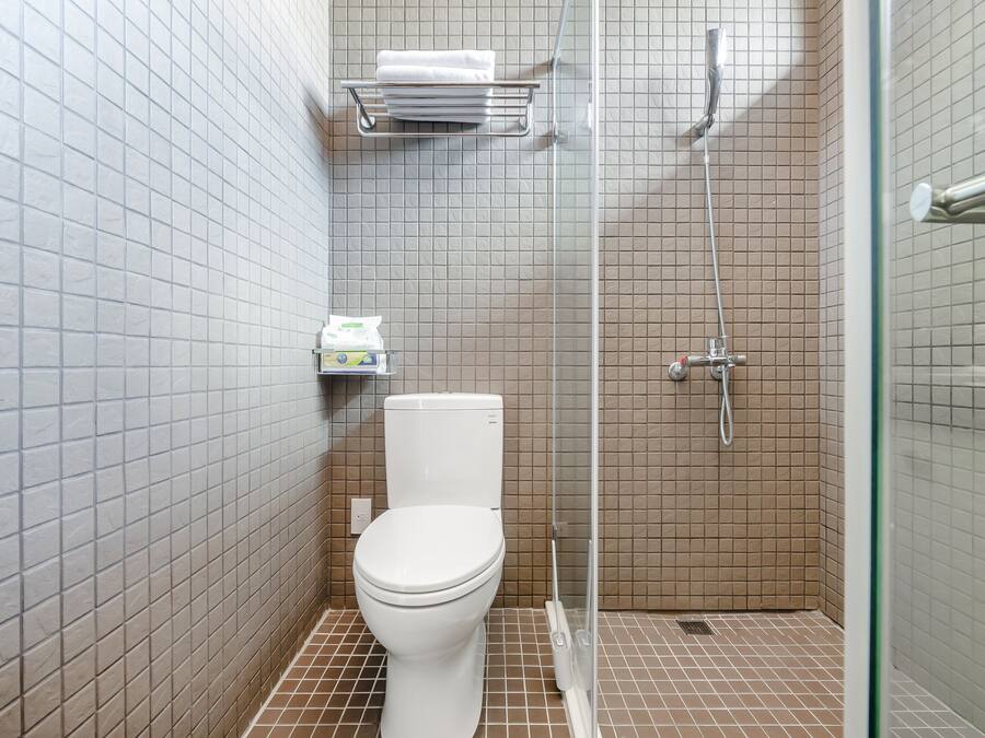A small, tiled bathroom with a toilet, a shower, and a shelf with toiletries.