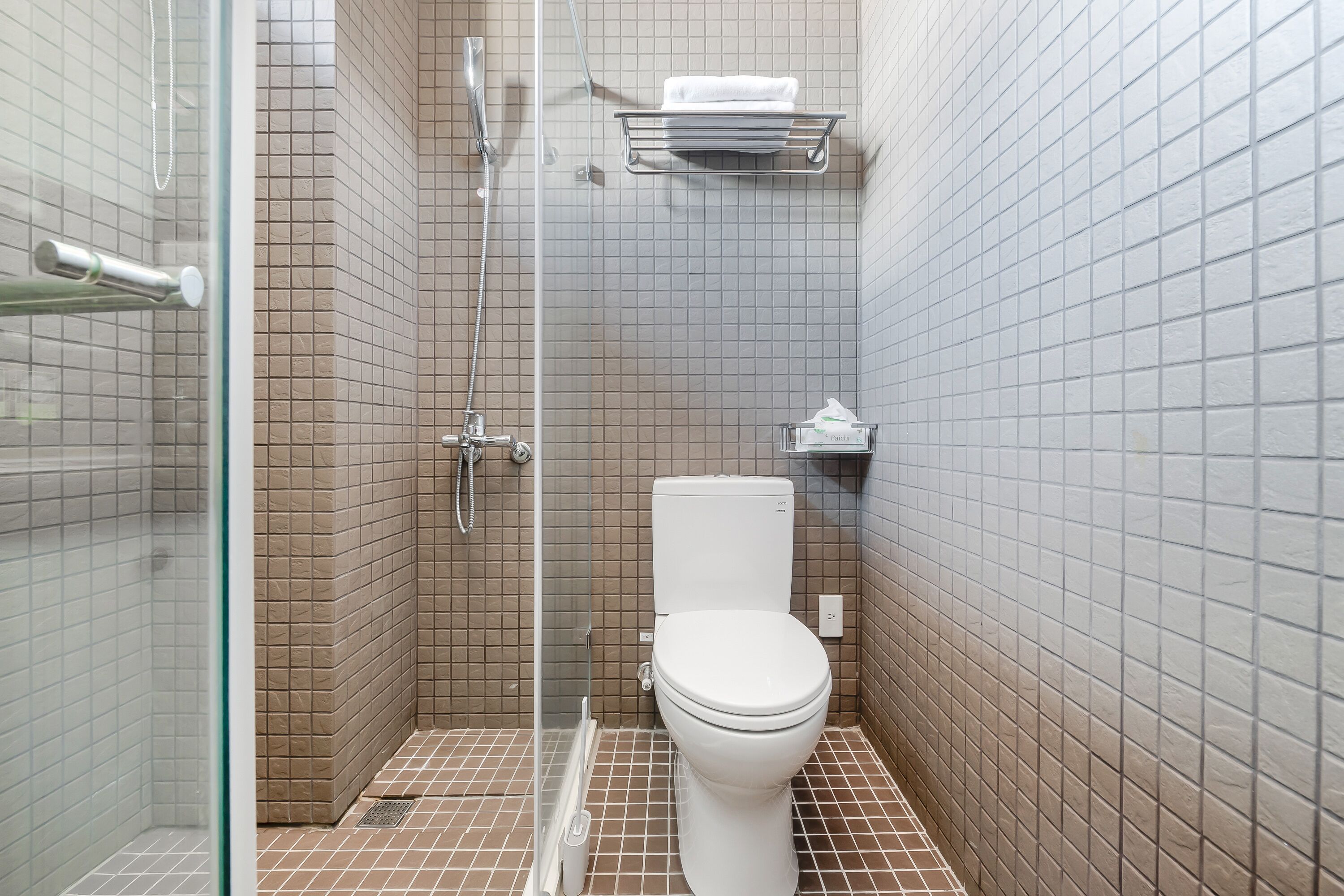 Un baño pequeño con azulejos, un inodoro, una ducha y zona de ducha con paredes de vidrio.