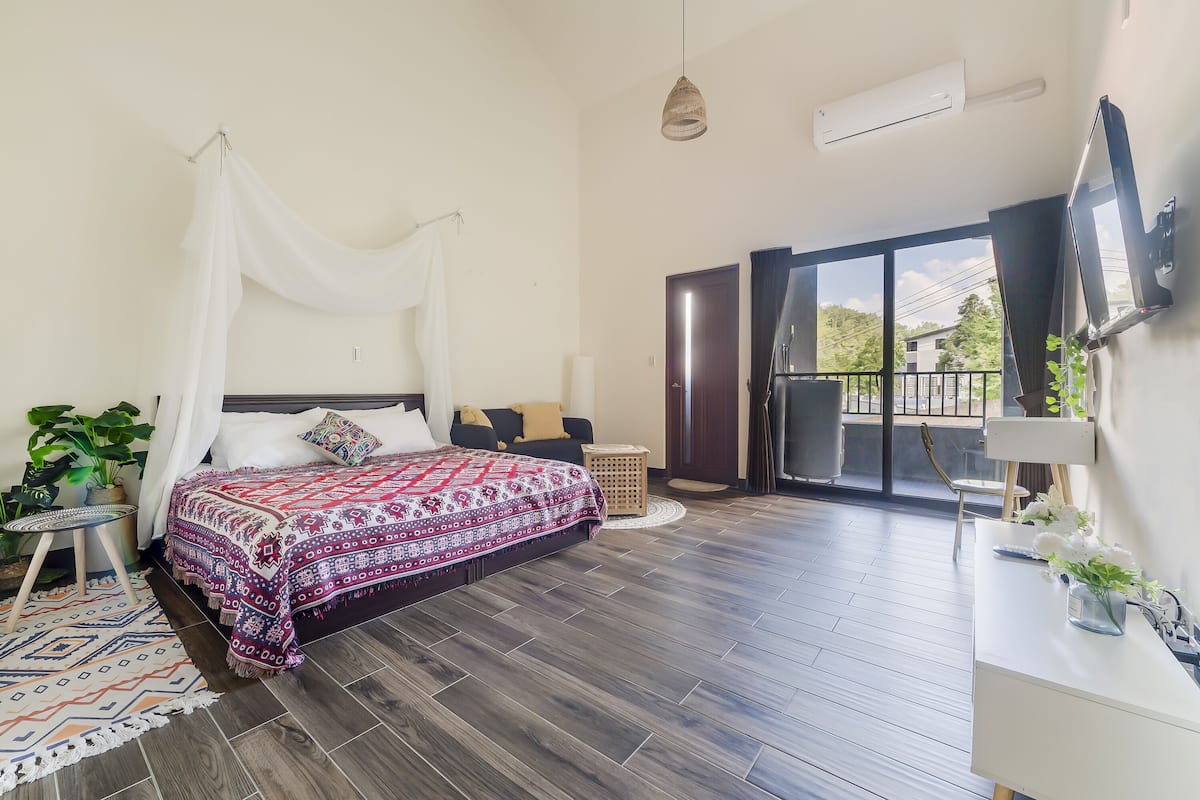 A bedroom with a bed, a TV, a desk, and a balcony.