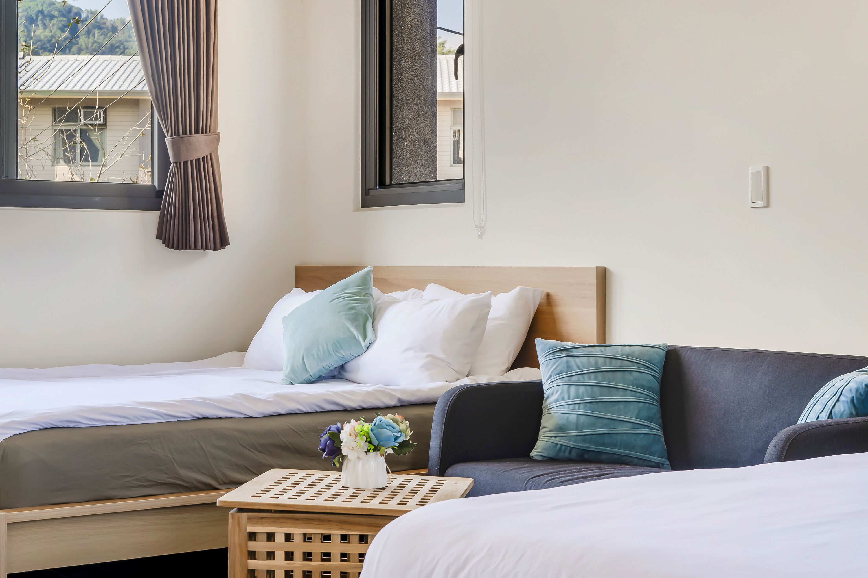Une chambre à coucher avec un lit, un canapé, une petite table sur laquelle est posé un vase de fleurs, et une fenêtre avec des rideaux.