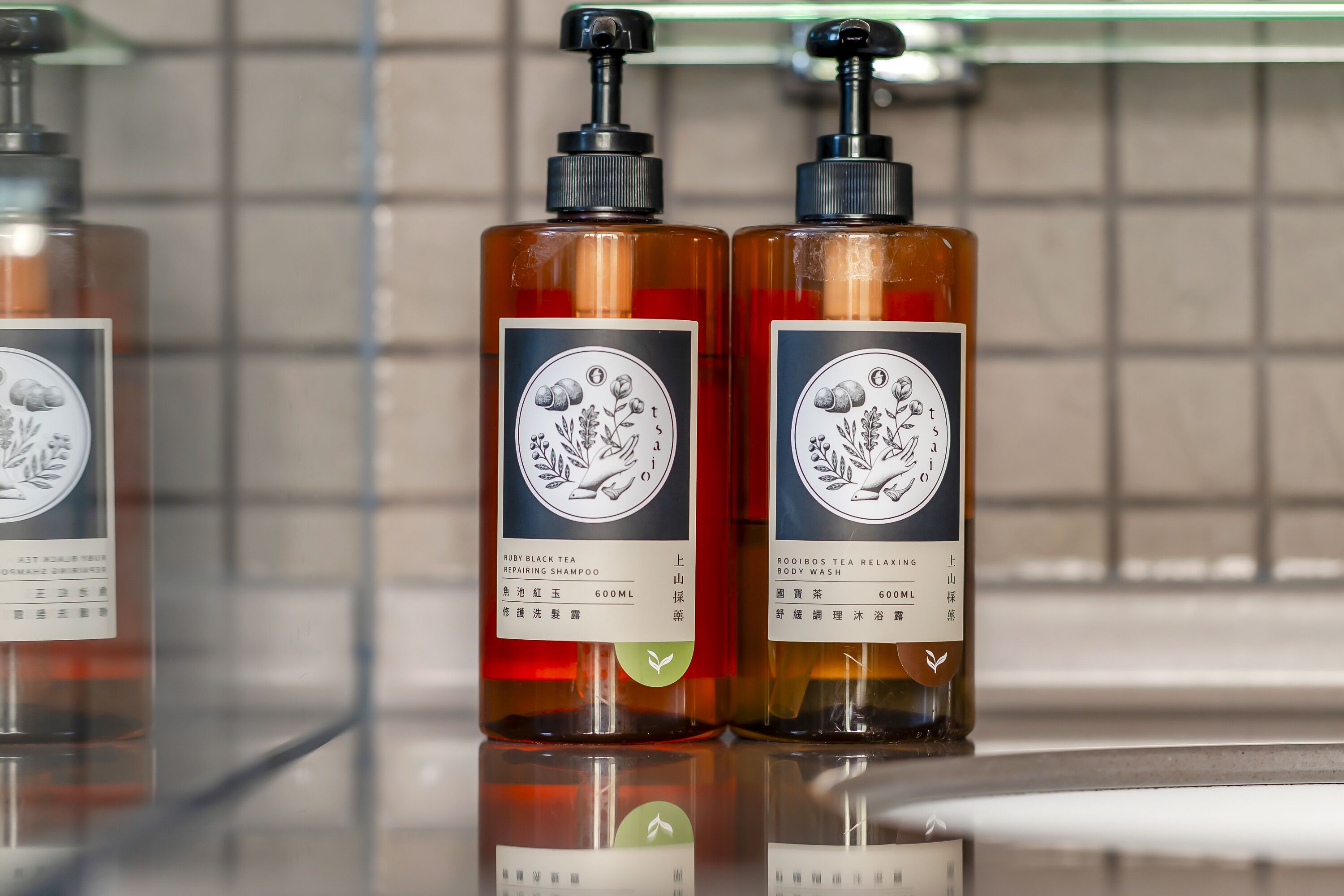 Two bottles of tea-based body wash and shampoo on a reflective surface.