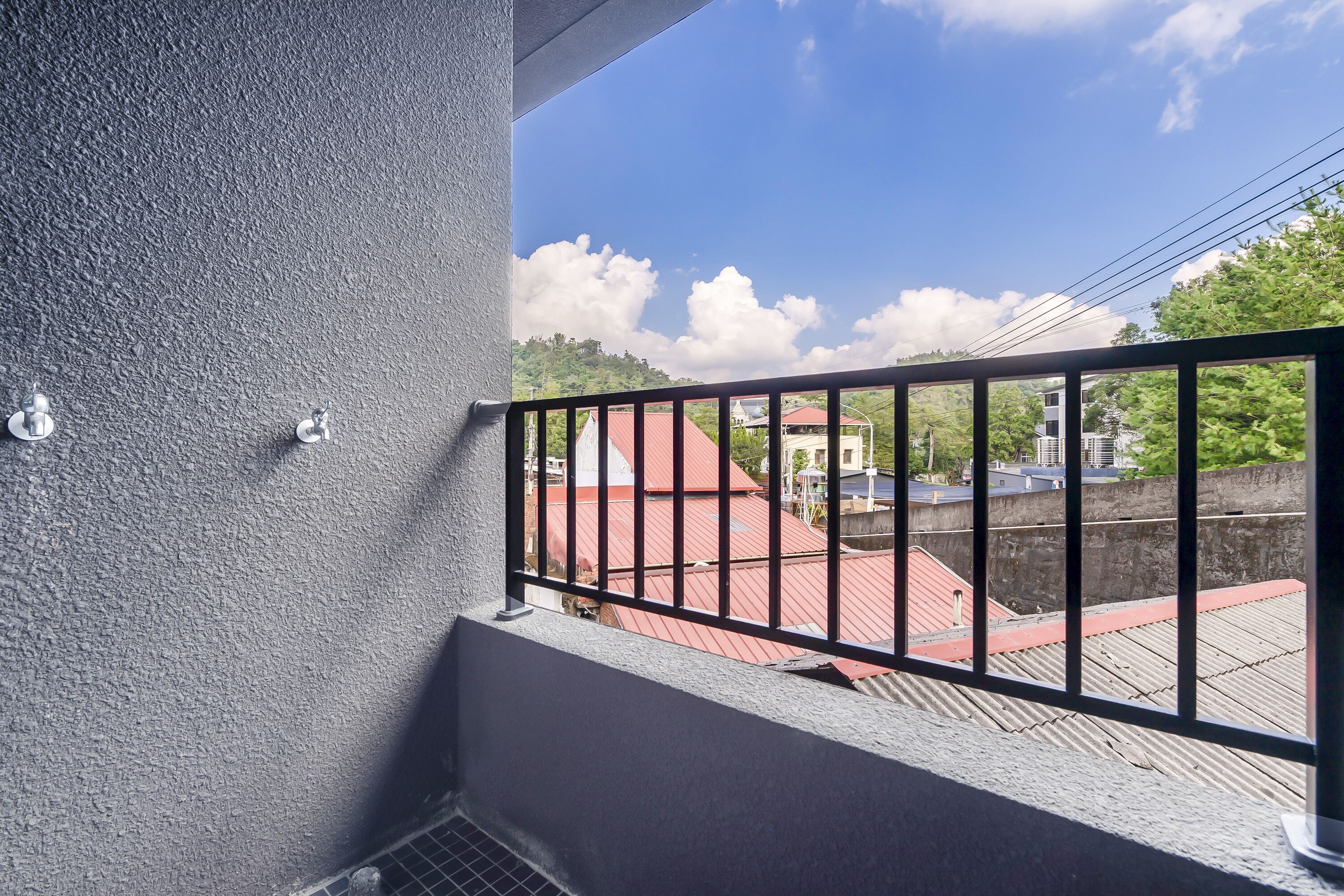 A balcony with a metal railing, a textured wall, and a view of buildings with red roofs.