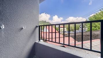 A balcony with a metal railing, a textured wall, and a view of buildings with red roofs.
