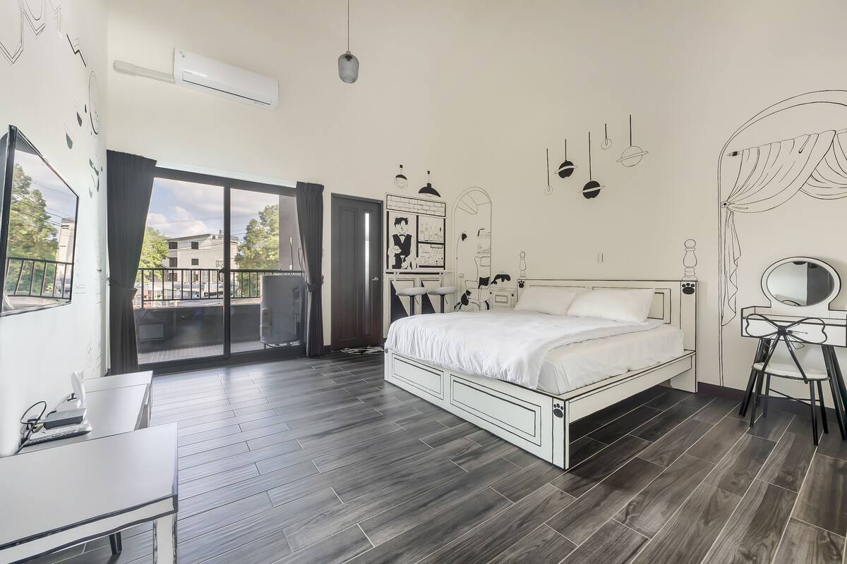 A modern bedroom with a large bed, a desk, and a wardrobe.