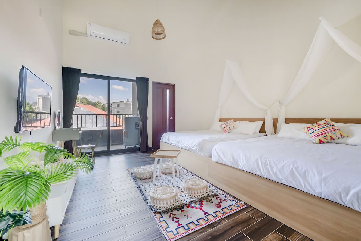 A bedroom with a bed, a bedside table, a chair, a potted plant, a window, and a view of the outside.