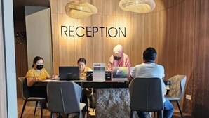 A reception area with a wooden wall, a reception desk, and three people seated at the desk. - Roxy Beach Apartment (Lundu)
