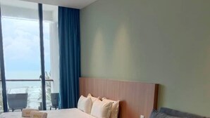 A modern hotel room with a large bed, a grey sofa, and a view of the sea. - Roxy Beach Apartment (Lundu)