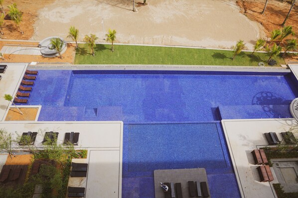 An aerial view of a swimming pool with a blue surface, surrounded by a grassy area and palm trees.