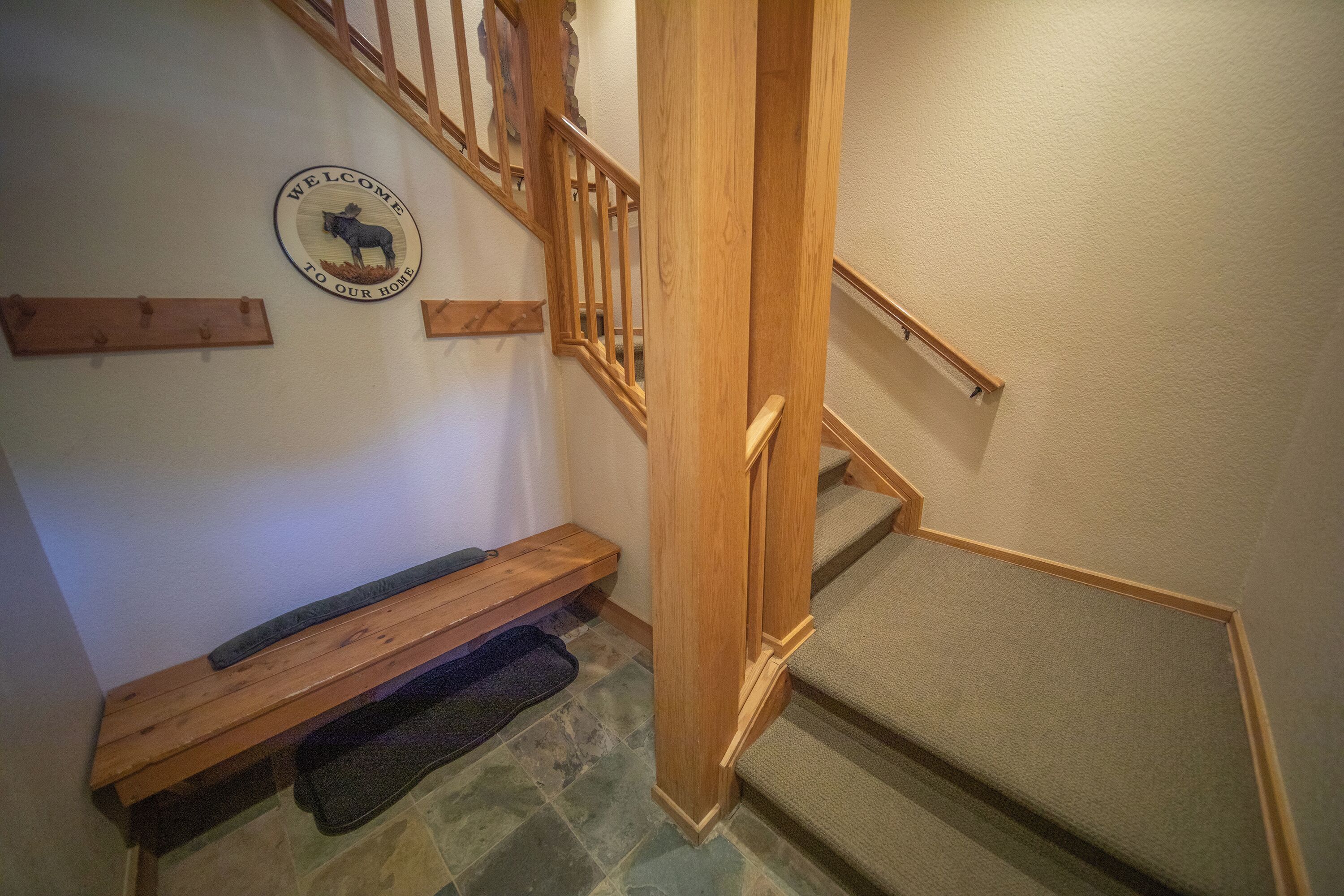 Una escalera de madera con barandilla de madera, un banco de madera y un cartel de bienvenida en la pared.