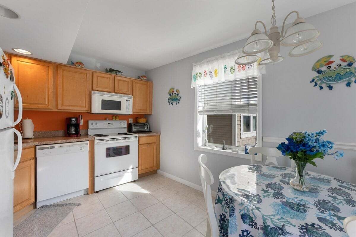 A kitchen with wooden cabinets, a white microwave, a stove, and a dining table with a floral tablecloth.