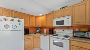 Una cocina con armarios de madera, un refrigerador blanco, un microondas, una estufa y un tostador.